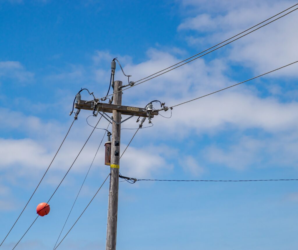 Wooden power line with wires and orange marker ball against a clear blue sky.