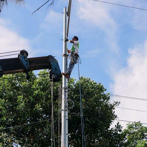 A utility worker climbs a pole for maintenance under a clear sky, showcasing safety and skill.